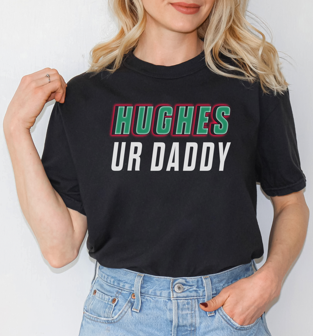 Person wearing a black t-shirt with 'HUGHES UR DADDY' text, standing against a plain background.