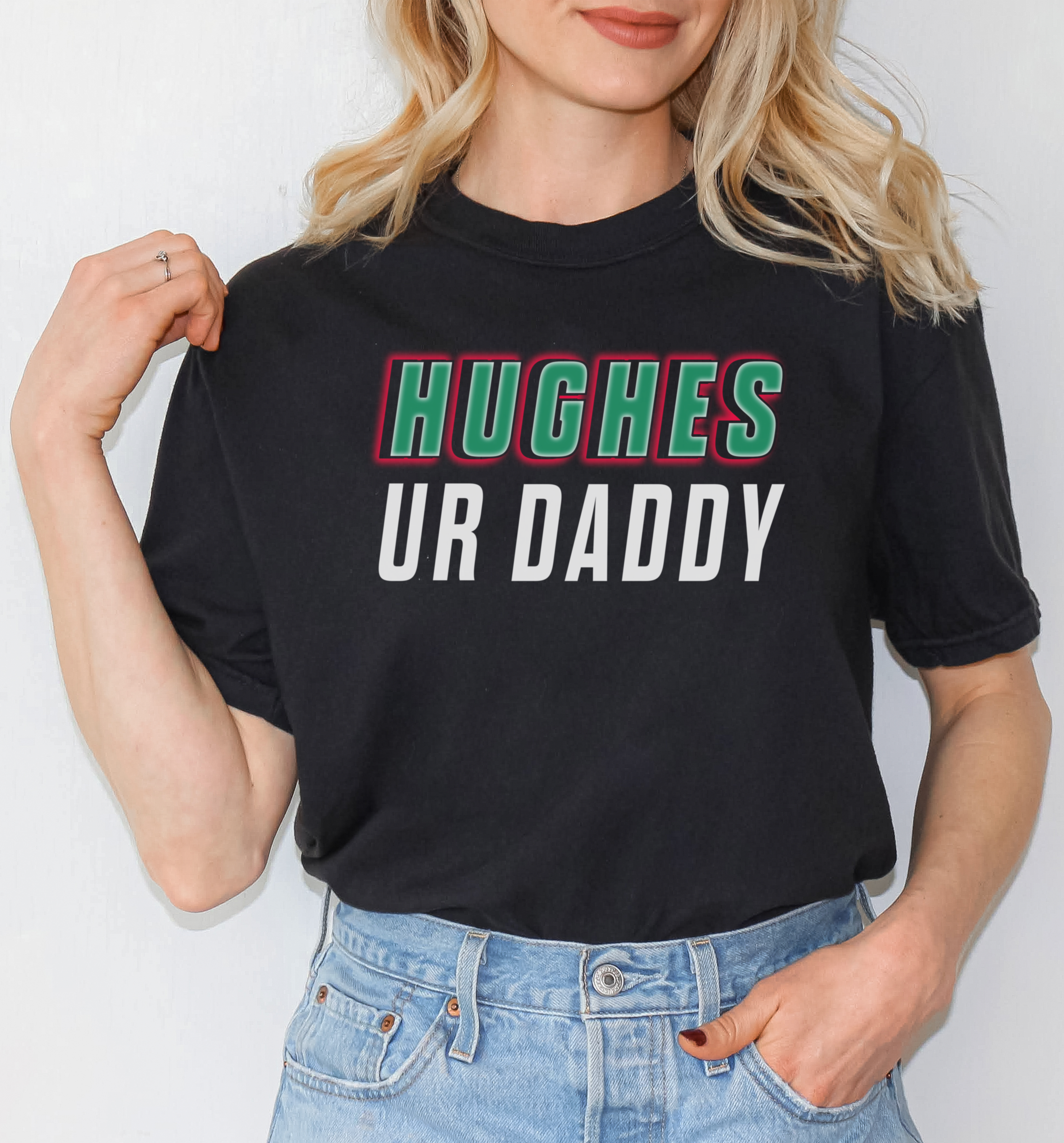 Person wearing a black t-shirt with 'HUGHES UR DADDY' text, standing against a plain background.